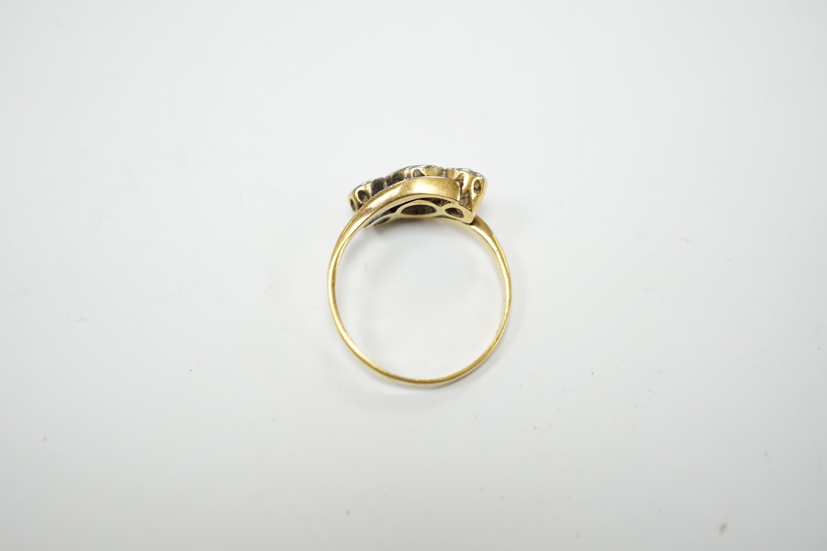 A yellow metal and illusion set three stone diamond set crossover ring, size O/P, gross weight 3.2 grams.